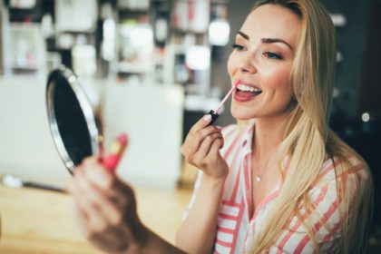 Beautiful young woman applying lips makeup