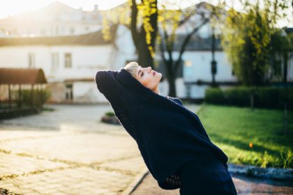 Fashion portrait of a stylish woman in an oversized sweater outdoors in the rays of the setting sun.