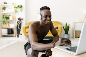 Happy young african man searching training video fitness program on laptop