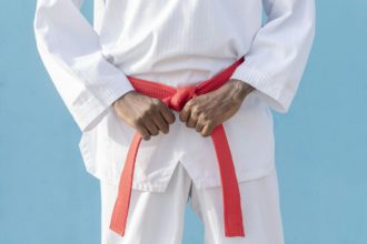 Man in martial arts uniform holding his red belt with both hands on a blue background