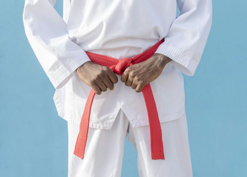 Man in martial arts uniform holding his red belt with both hands on a blue background